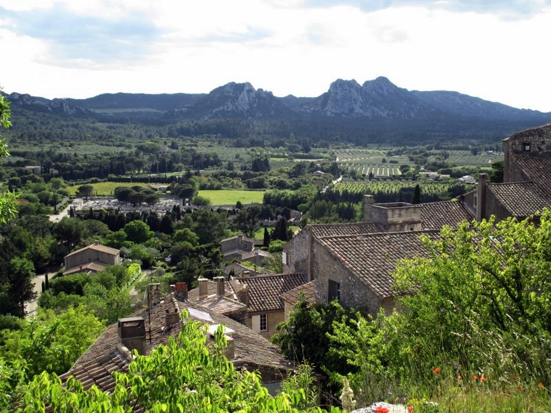 A scenic view of a lush valley from an elevated hillside village, showcasing traditional stone buildings in the foreground and rolling hills with rocky peaks in the background.